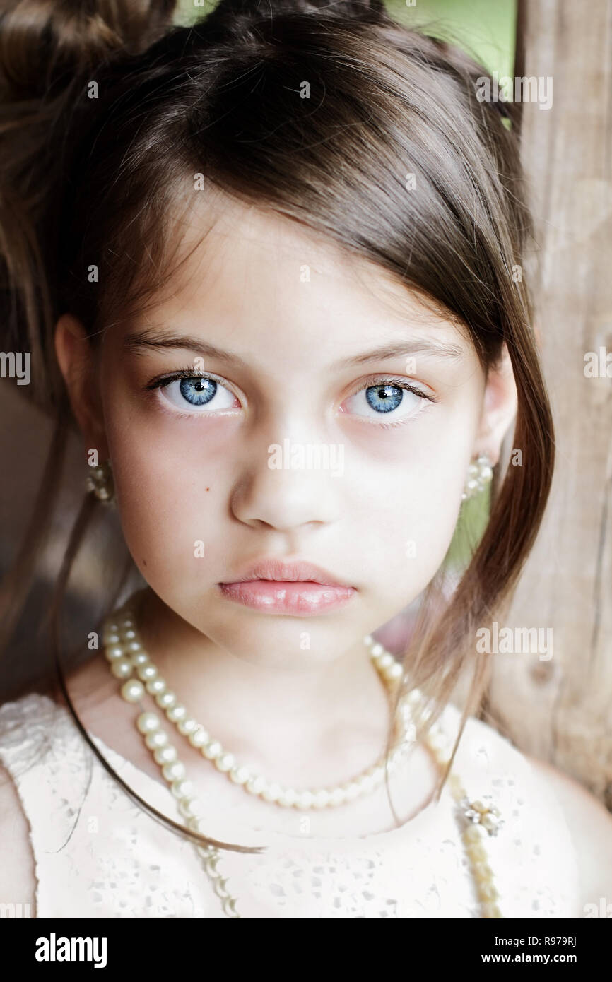 Young girl looking directly into the camera, wearing vintage pearl necklace and hair pulled back. Extreme shallow depth of field with selective focus  Stock Photo