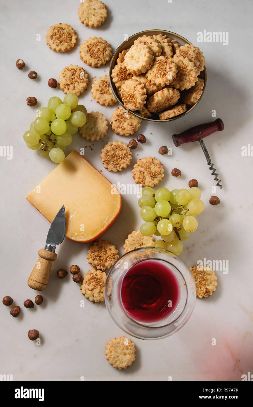 Wine snack. Cheese, grapes, nuts, cheese crackers cookies with glass of red wine and knife over white marble background. Flat lay, space Stock Photo