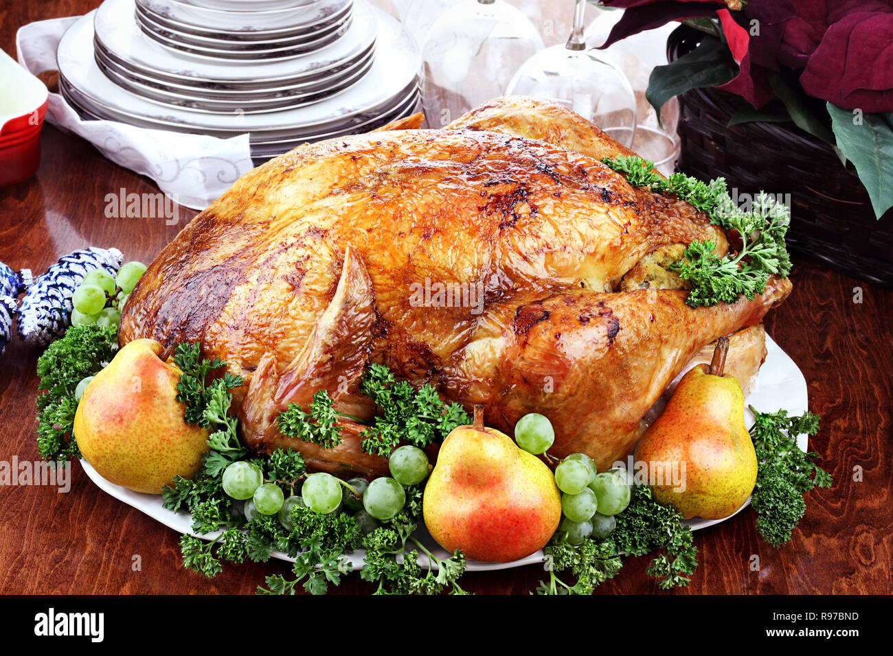 Thanksgiving or Christmas turkey dinner with fresh pears, grapes and parsley. Poinsettia flower arrangement, dishes and wine glasses in background. Stock Photo