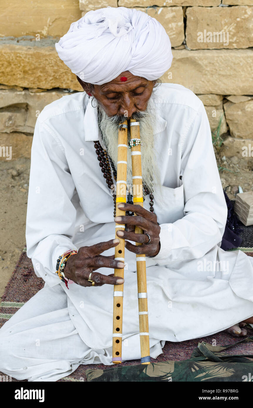 Old Indian man in traditional white clothing playing double flutes in Jaisalmer desert, Jaisalmer, Rajasthan, India Stock Photo