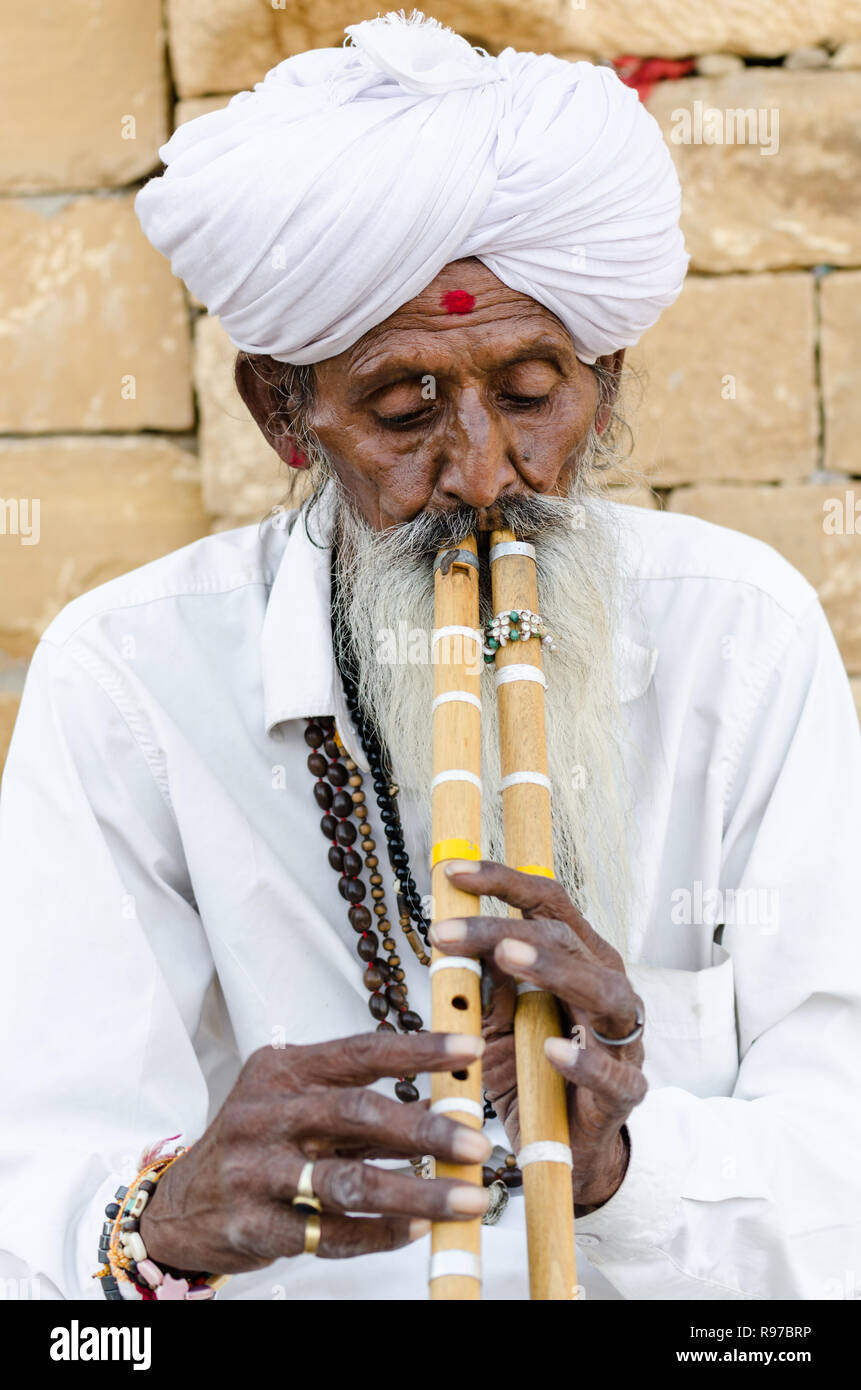 Old Indian man in traditional white clothing playing double flutes in Jaisalmer desert, Jaisalmer, Rajasthan, India Stock Photo