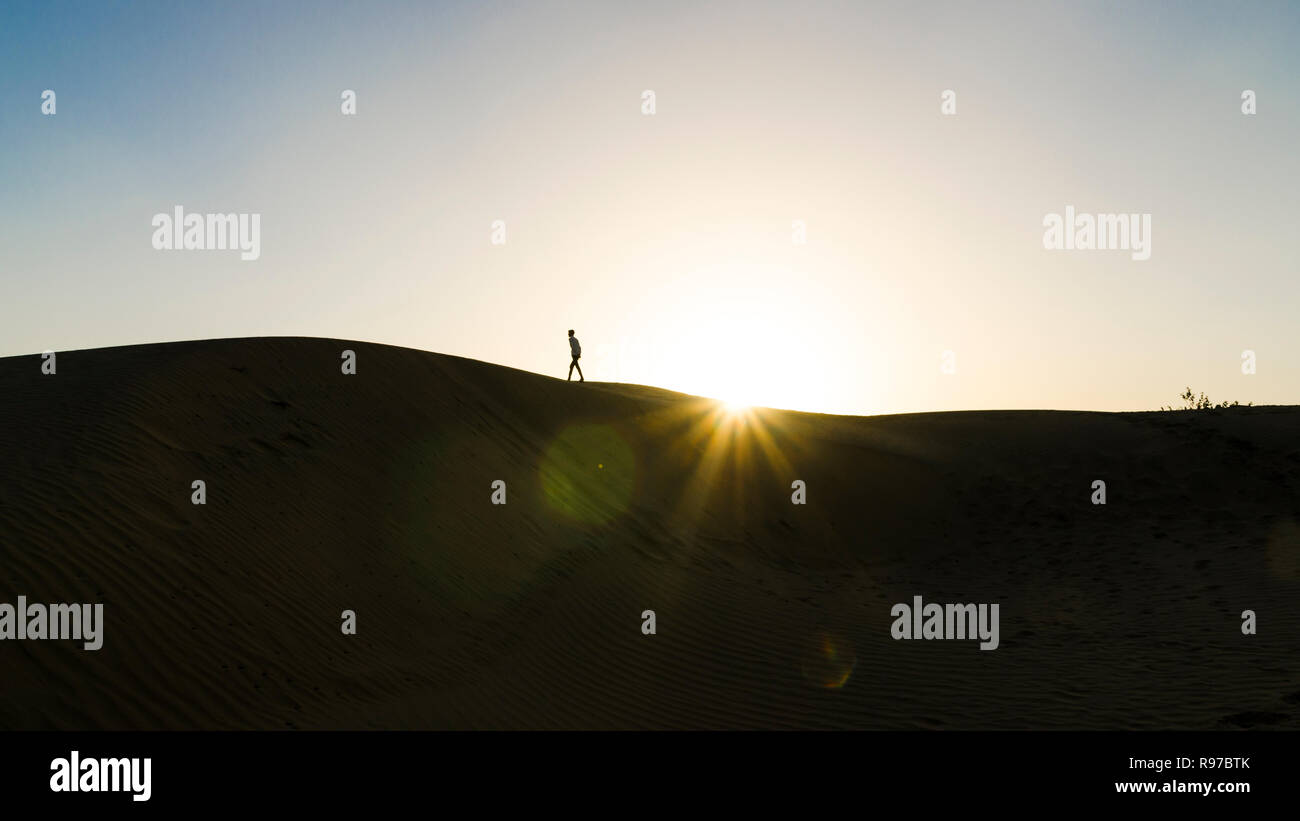 Silhouette of a man walking on a sand dune with sun setting down, Jaisalmer desert, Rajasthan, India Stock Photo