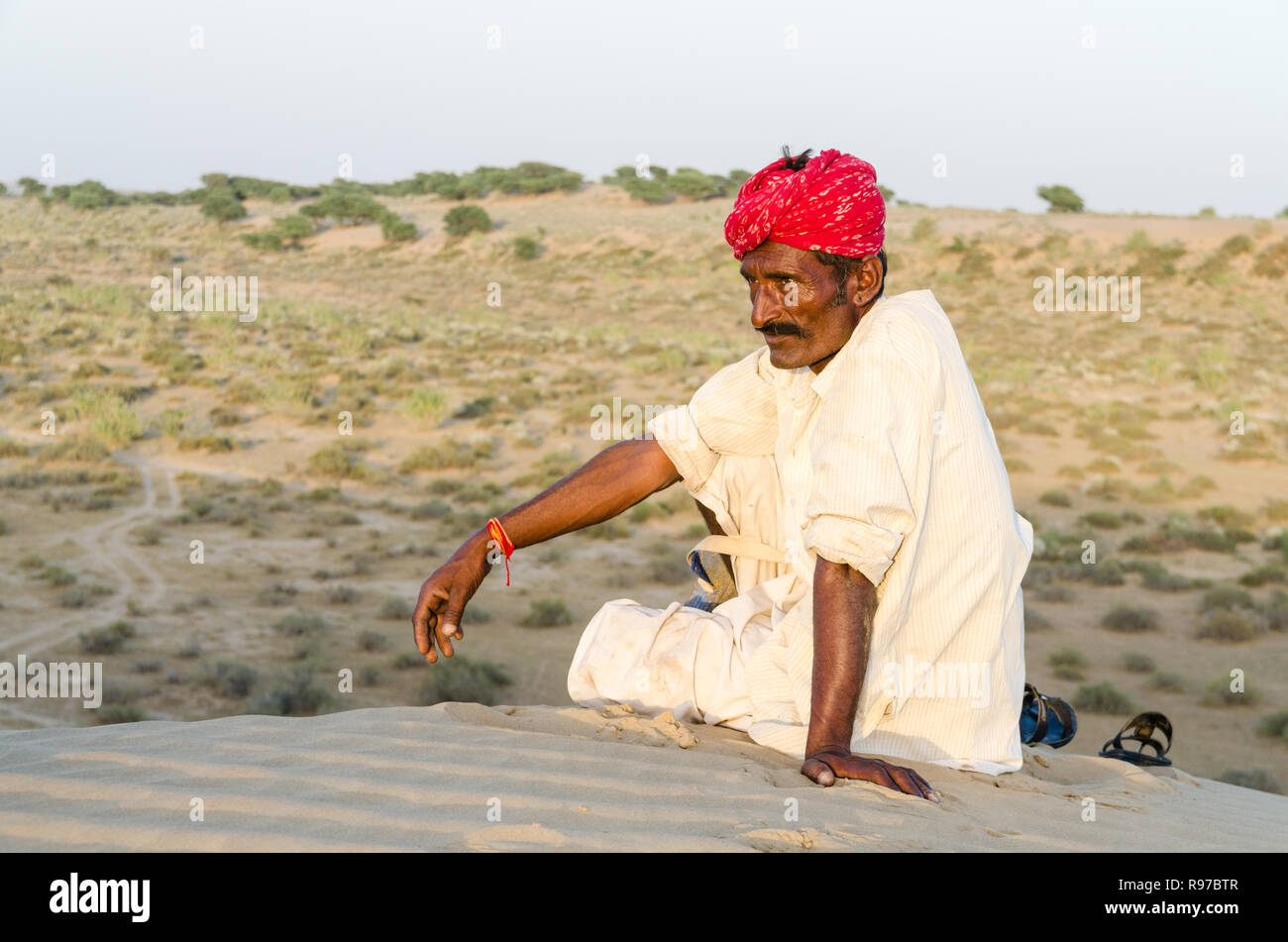 Local Indian man in traditional clothing sitting on a sand dune