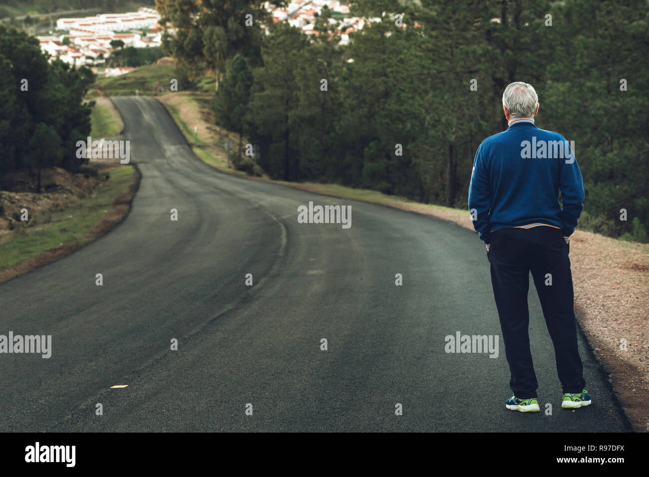 Active senior man standing on lonely road between mountains. Older man of back standing on lonely highway Stock Photo