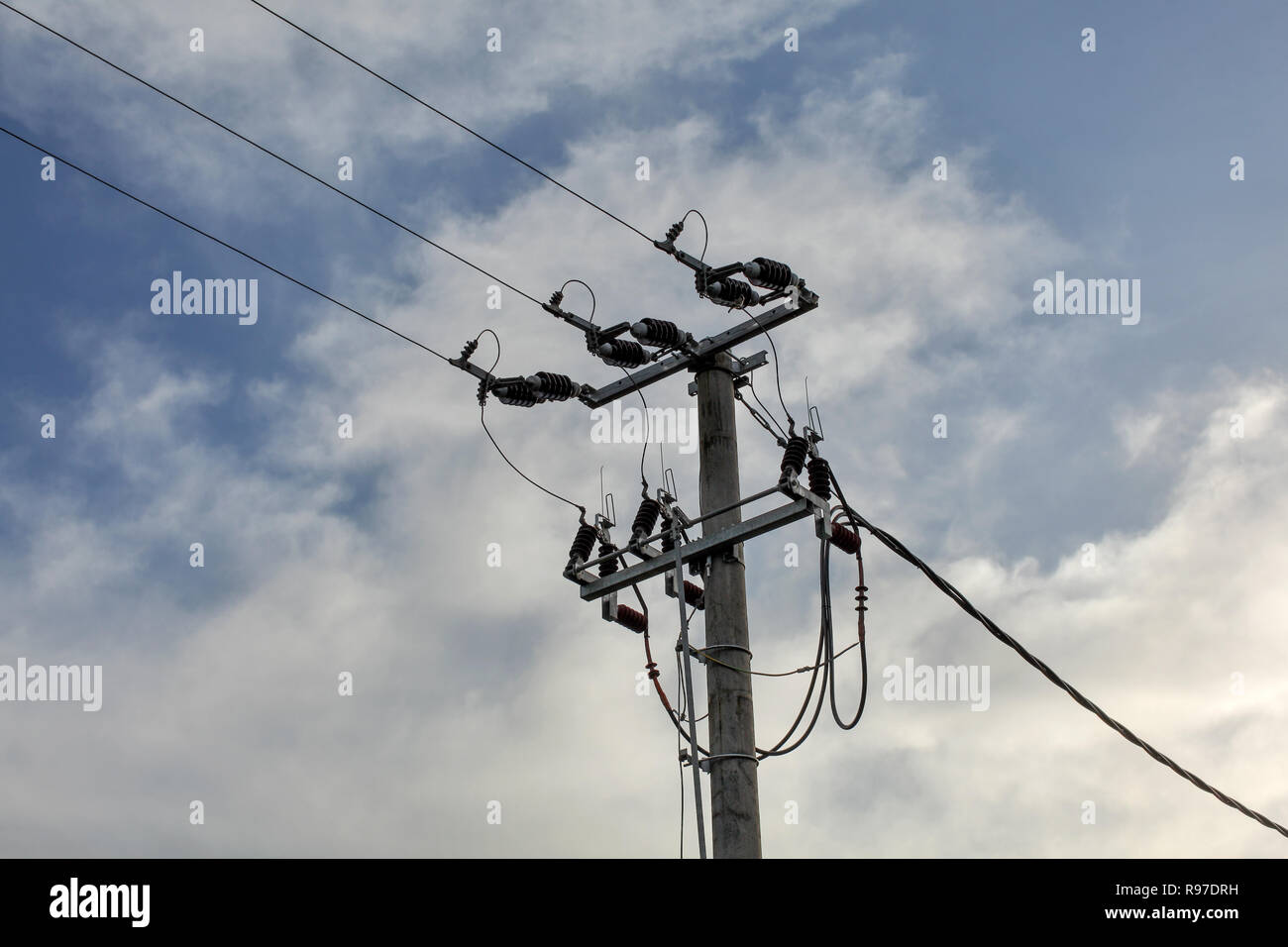 Small concrete pillar with power lines, sky with clouds in background. Stock Photo