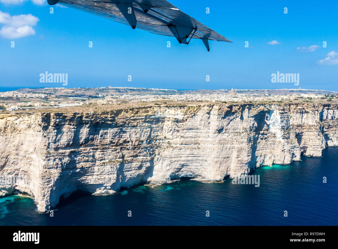 Gozo island from above, under the wing of a small plane. Aerial view of Gozo, Malta. The Rotunda of Xewkija (Casal Xeuchia) is the largest in Gozo island and its dome dominates the village. Stock Photo
