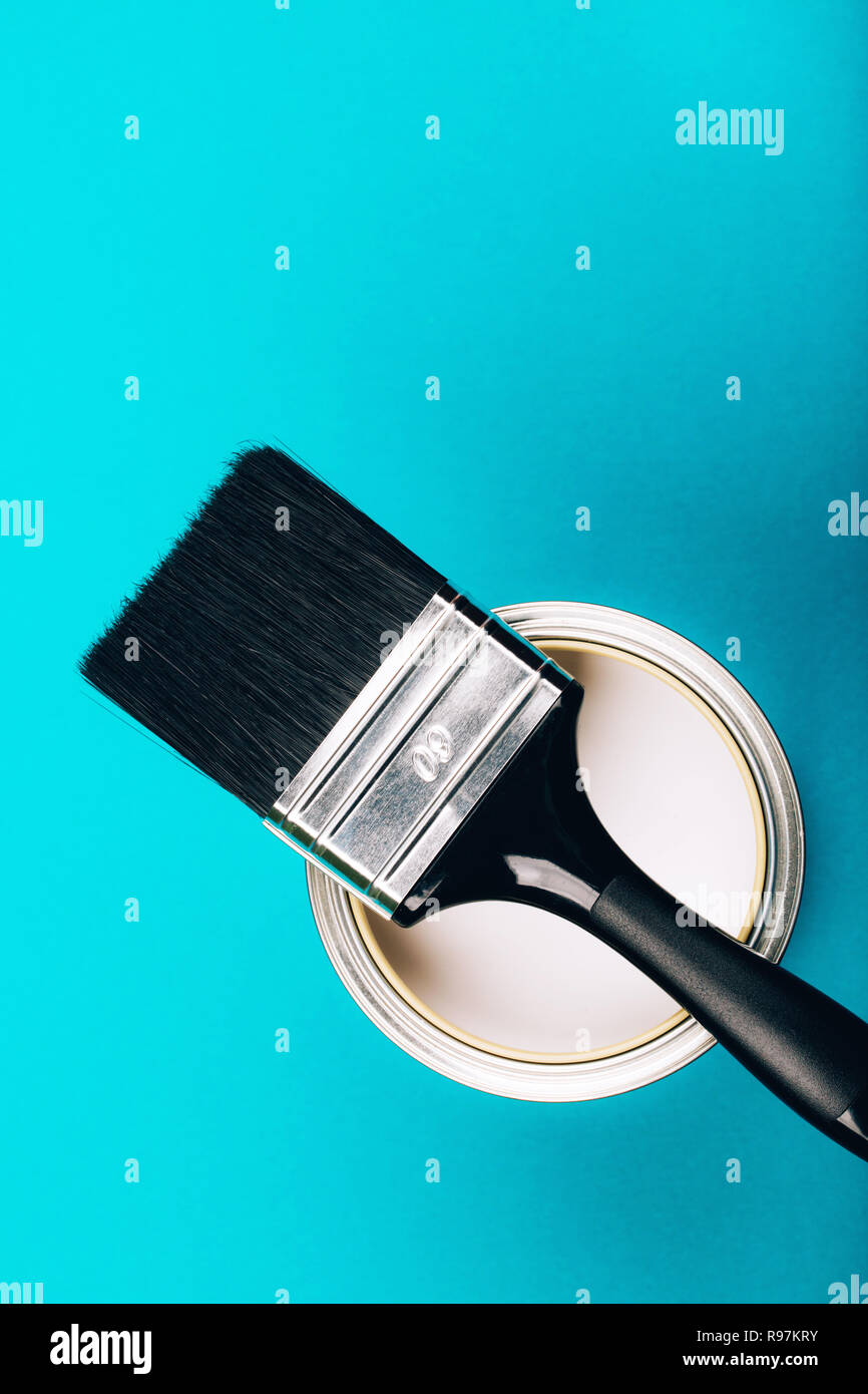Brush with black handle on open can of white paint on blue background ...