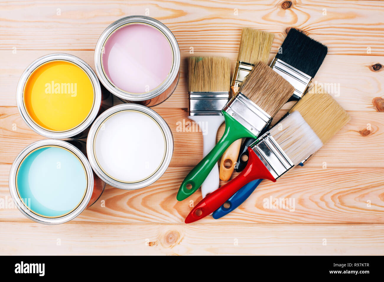 Four open cans of paint with brushes on natural wooden background. Yellow, white, pink, turquoise colors. Renovation concept. Stock Photo