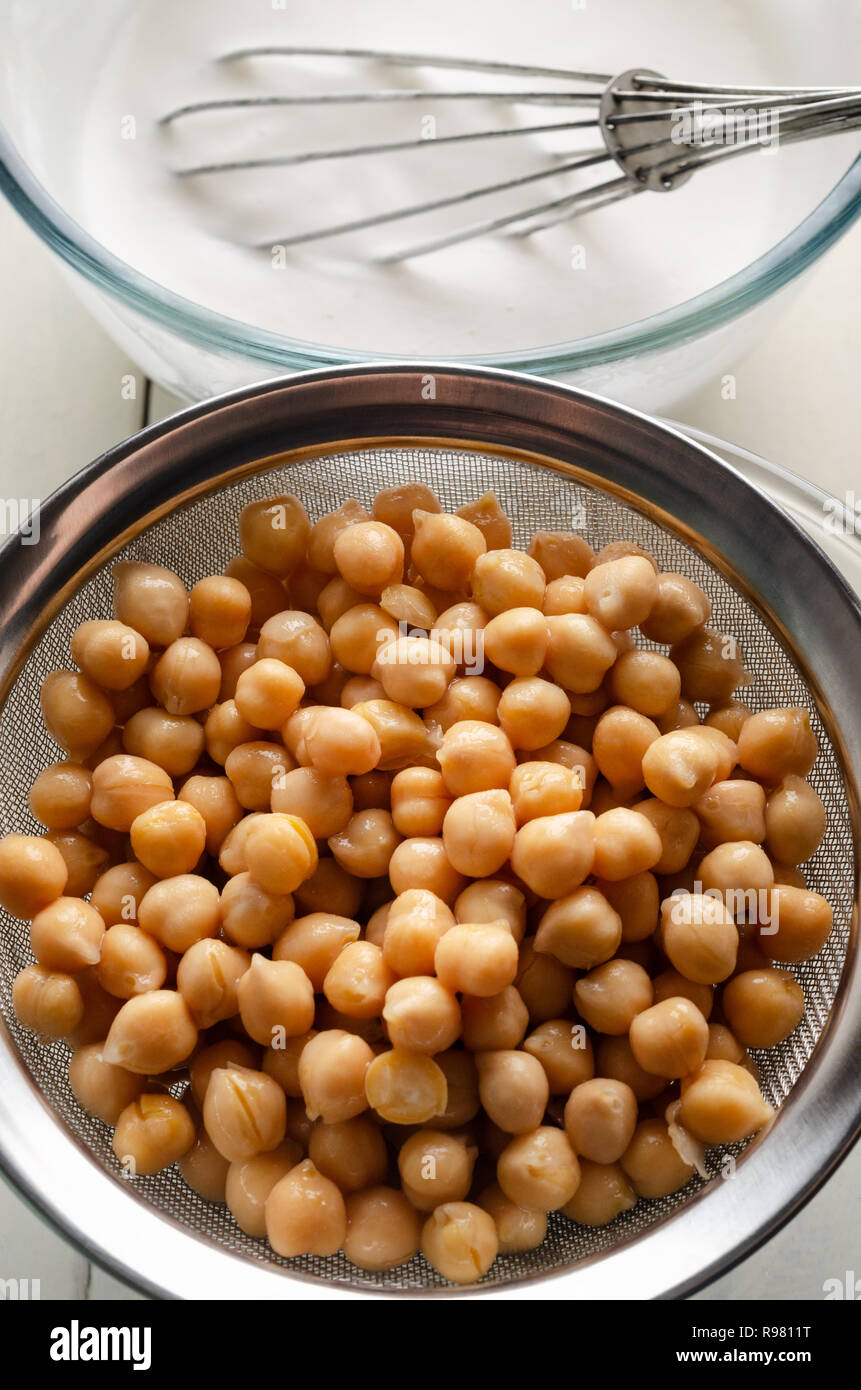 Overhead view of chickpeas draining in one bowl through a sieve and aquafaba in a second bowl, whisked to use as vegan egg replacer. Stock Photo