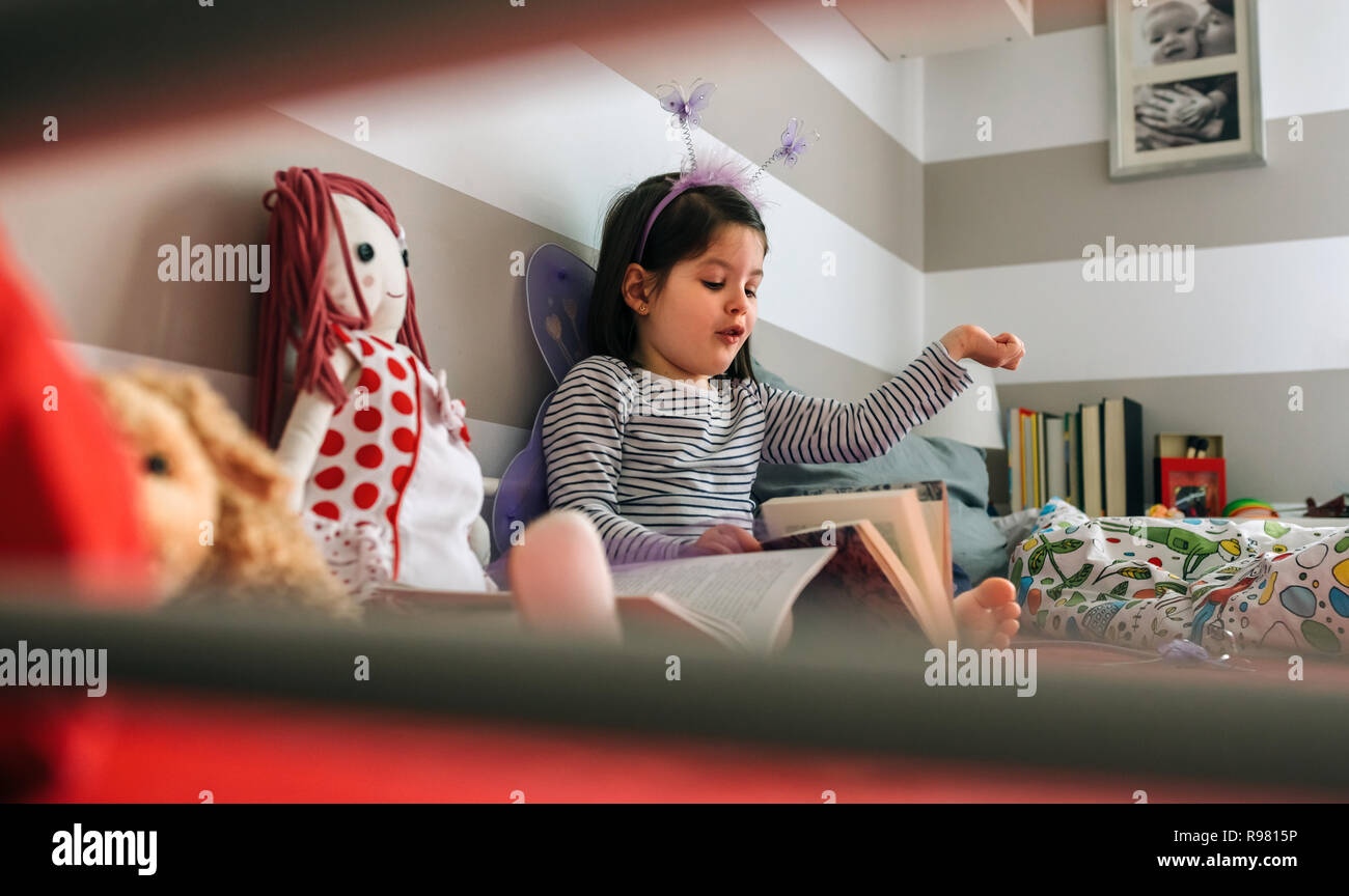 Girl disguised reading a book to her doll Stock Photo