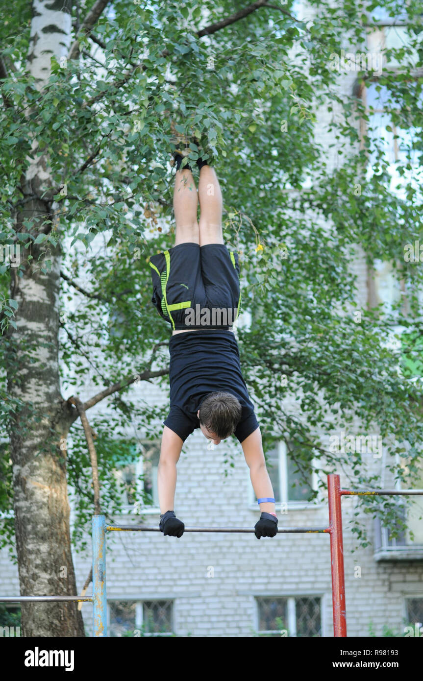 Kovrov, Russia. 11 August 2013. Teen is engaged in discipline gimbarr on a horizontal bar in the courtyard of a multi-storey residential building Stock Photo