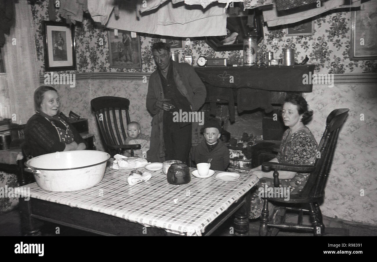 1940, a Welsh coal mine worker and his family around the fireplace, having a cup of tea at home in the front room at Merthyr, Wales. Stock Photo