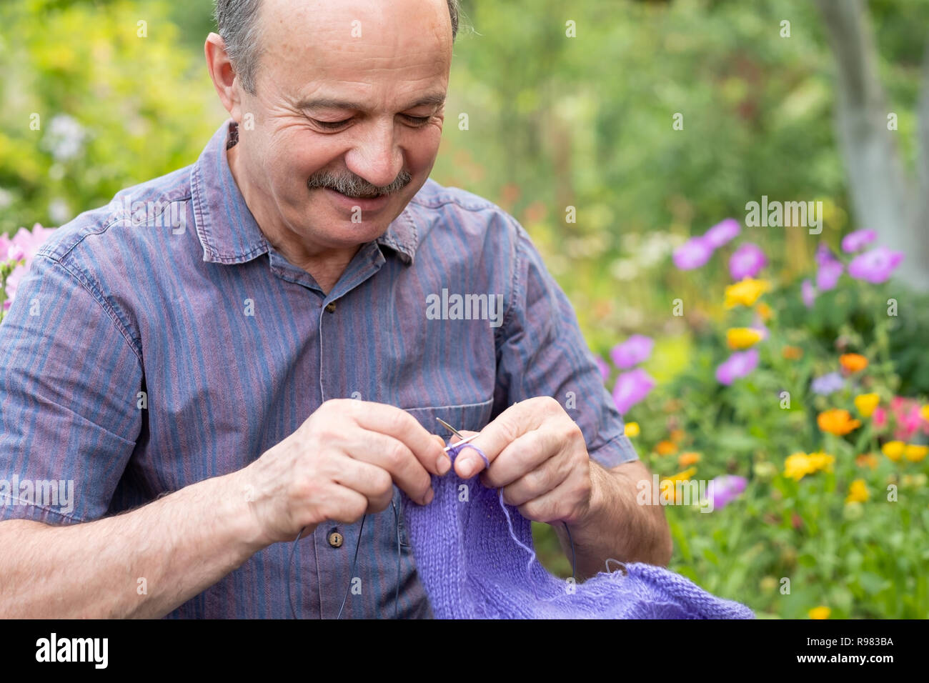 Old handsome man sitting at his summer garden with the knitting needles. Stock Photo