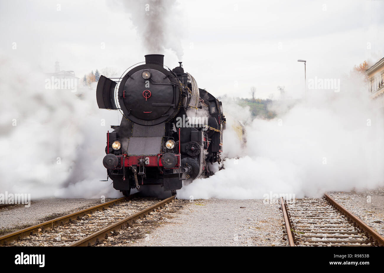 Old steam train leaving the station in Nova Gorica, Slovenia, Europe. Lots of black and gray steam hiding the locomotive. Stock Photo