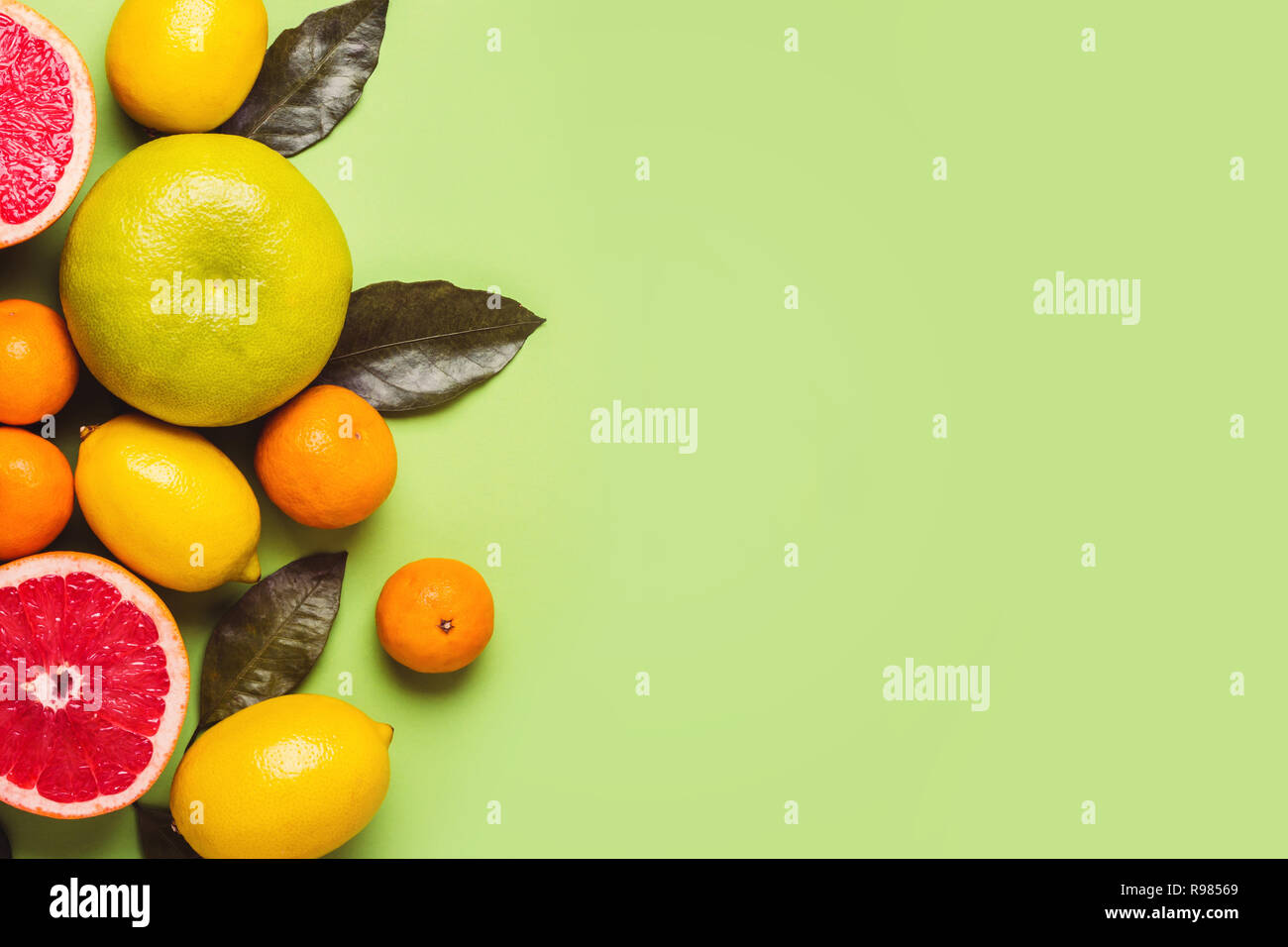Grapefruits and lemons with leaves on a green background. Rich harvest concept. Stock Photo