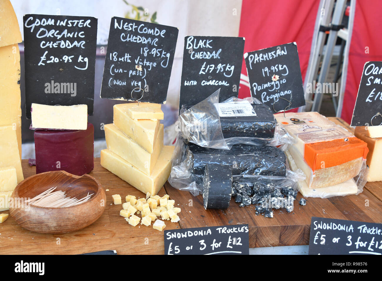 Cheeses on market stall in Somerset displayed with samples for tasting.Godminster Organic Cheddar,Westcombe Cheddar,Black Cheddar,Parmesan. England,UK Stock Photo