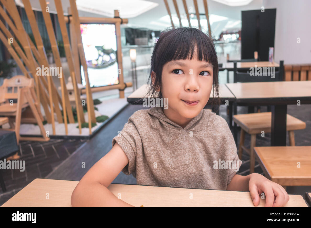 Hungry Funny child licking her lip waiting for food in restaurant. Stock Photo