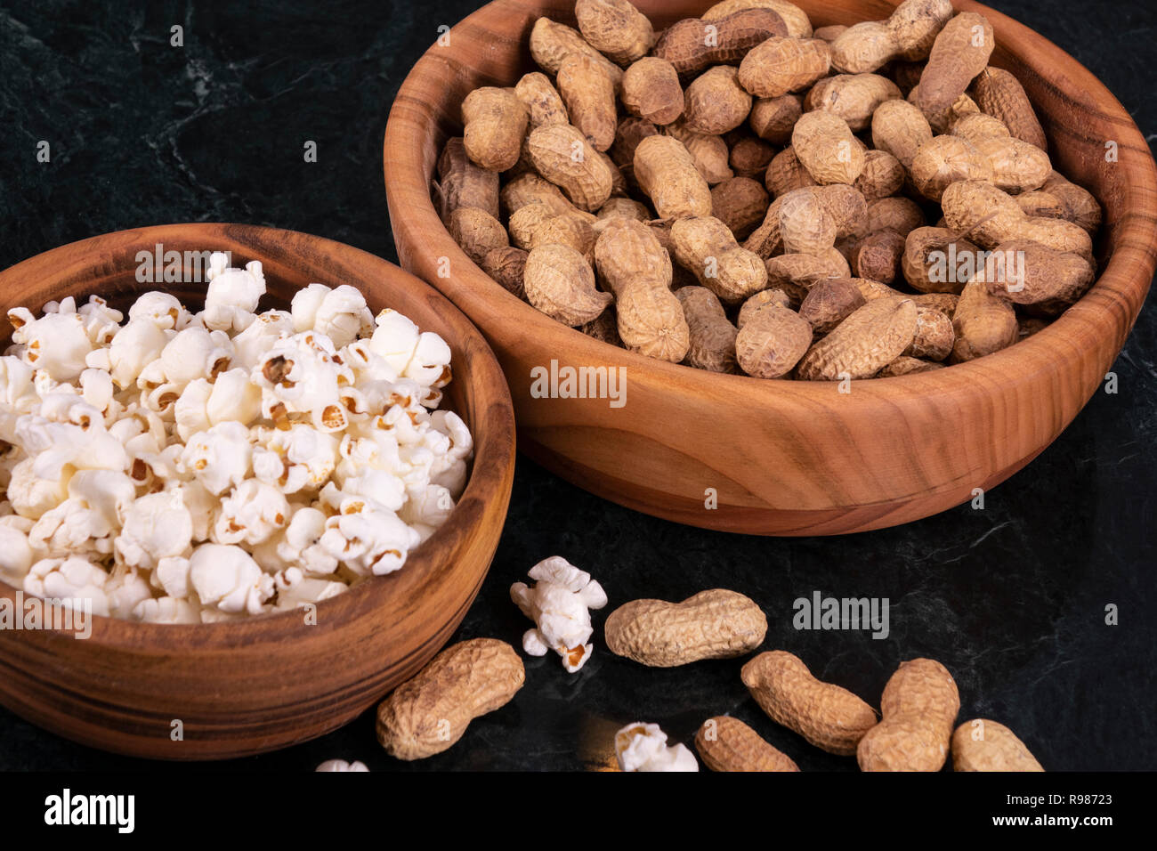 Peanuts with Popcorn in golden wood bowl on black marble table Stock Photo