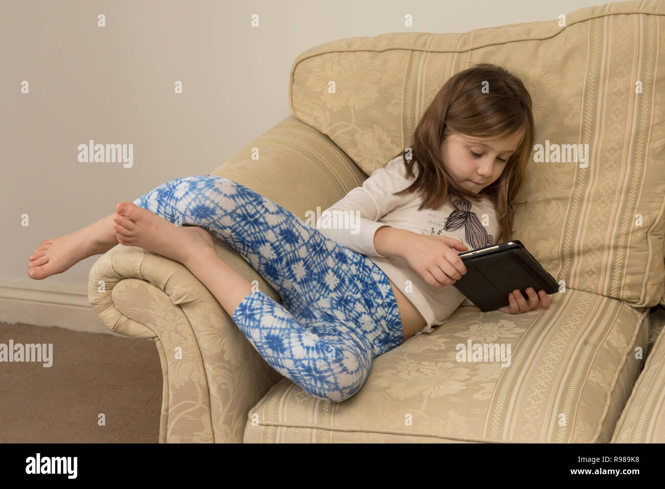 Young Girl Laying Of A Sofa Playing With An Ipad Digital Device