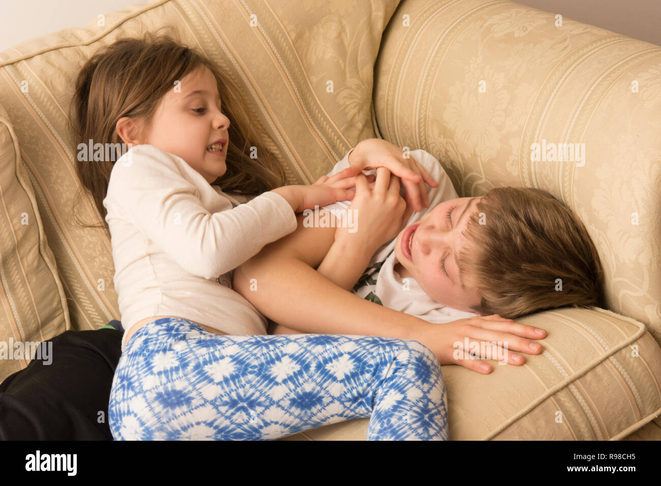children, boy and girl, brother and sister, siblings, play-fighting, fighting, wrestling, noisy, violent, on sofa, twelve years old, six years old. Stock Photo