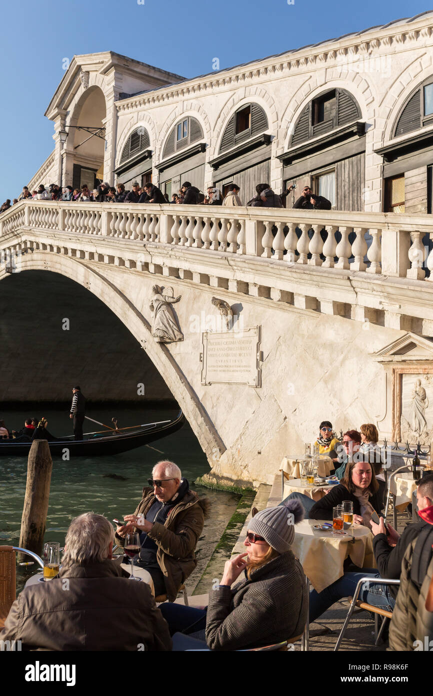 Venice, Italy - March 21, 2018: Tourists sitting at outdoor cafe near the famous Rialto bridge at Grand Canal in Venice, Italy Stock Photo