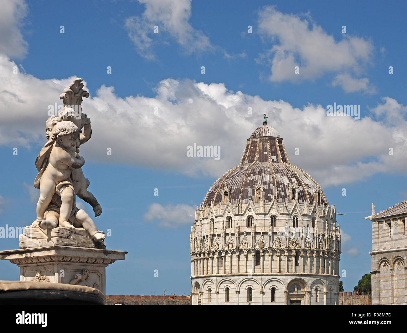 statue of cherubs with the Baptistery (Baptistery of San Giovanni) Pisa, on the Piazza dei Miracoli (Square of Miracles) in Pisa Tuscany, Italy Stock Photo