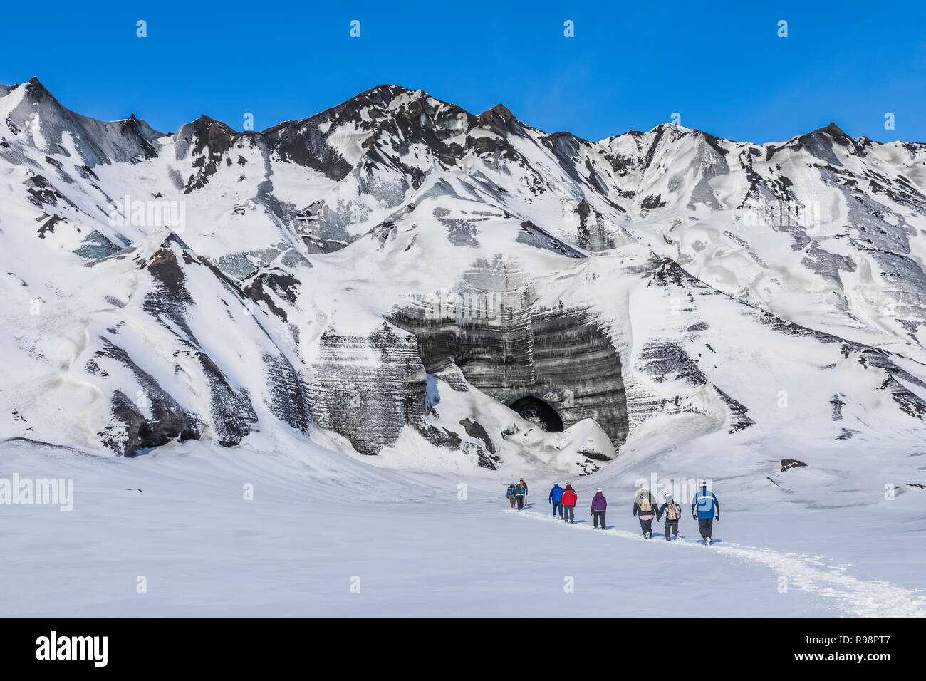 Adventurers walking toward an ice cave entrance in a lobe of Mýrdalsjökull Glacier, which sits atop Katla Volcano, in winter in Iceland [No model rele Stock Photo