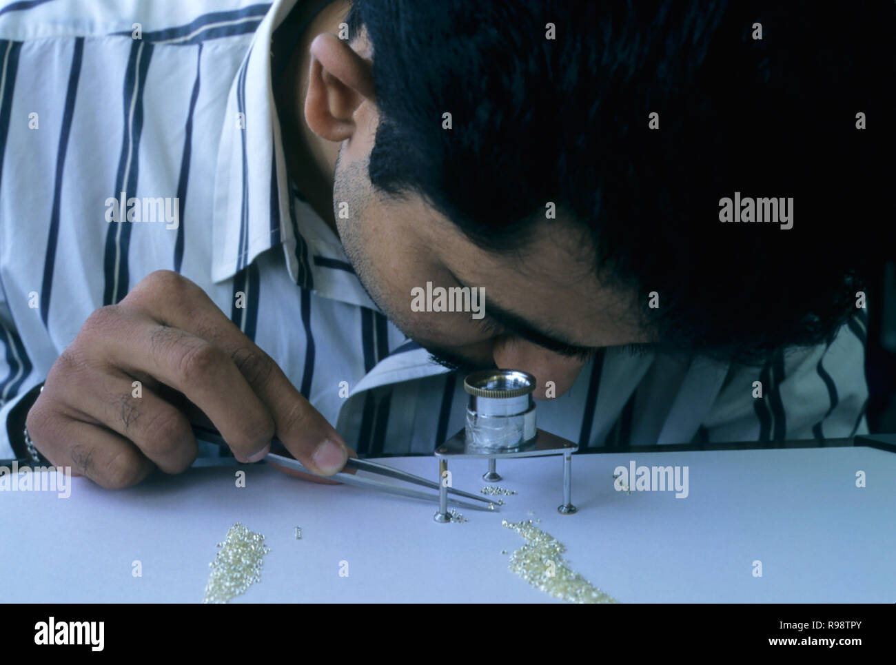 Man sorting grading looking at diamond through magnifying glass Stock Photo