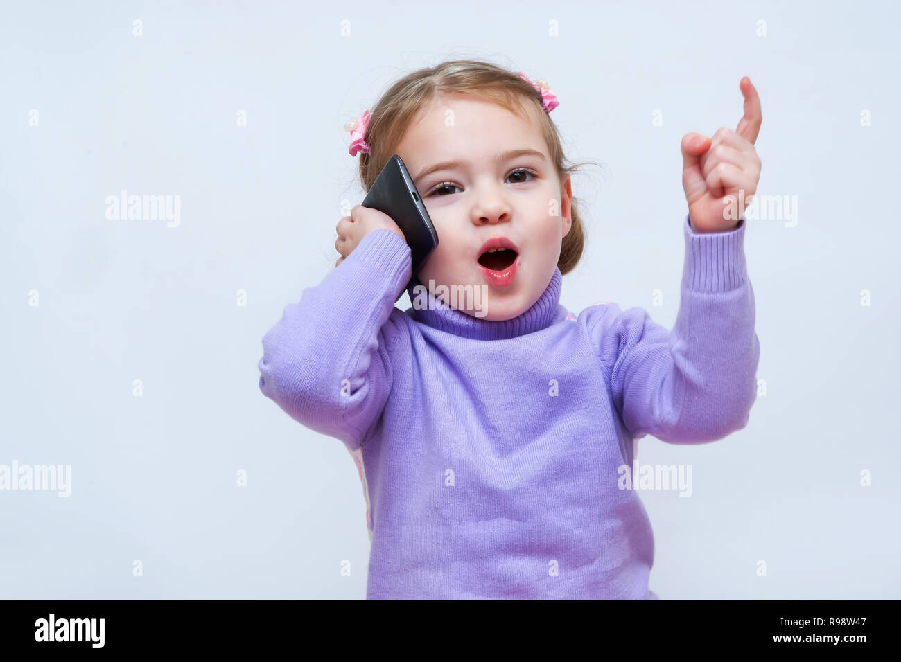 The beautiful little girl speaks on the phone and lifted her finger up Stock Photo