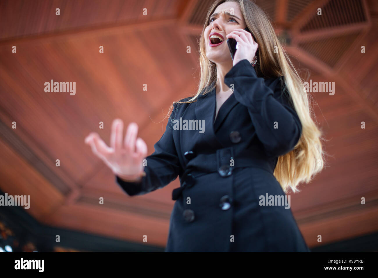 Beautiful young female in elegant outfit screaming and gesturing while being fired from work by phone in park Stock Photo