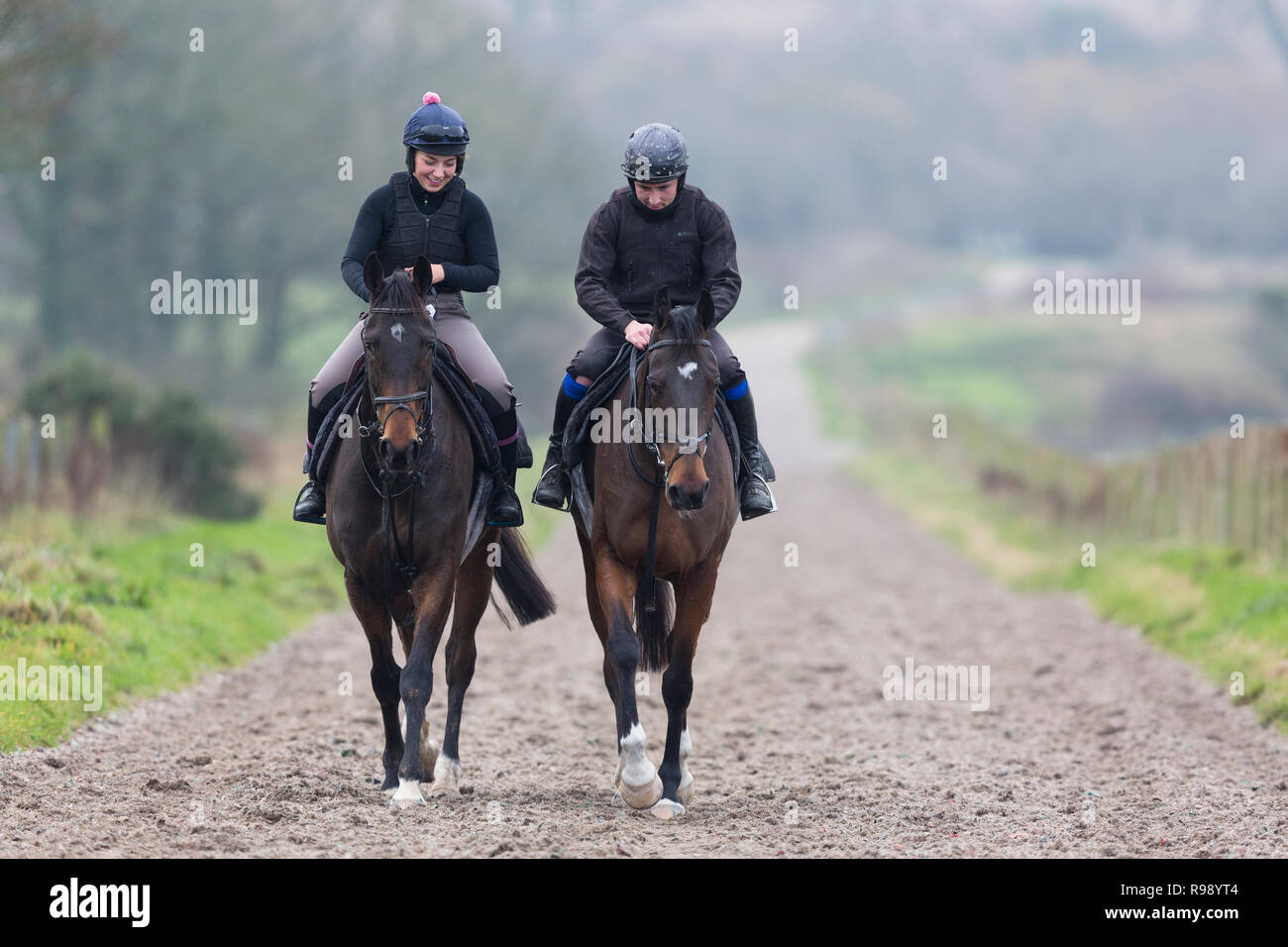 A man and woman ride horses after exercising them on the gallops at Peter Bowen Stables in Pembrokeshire, Wales Stock Photo