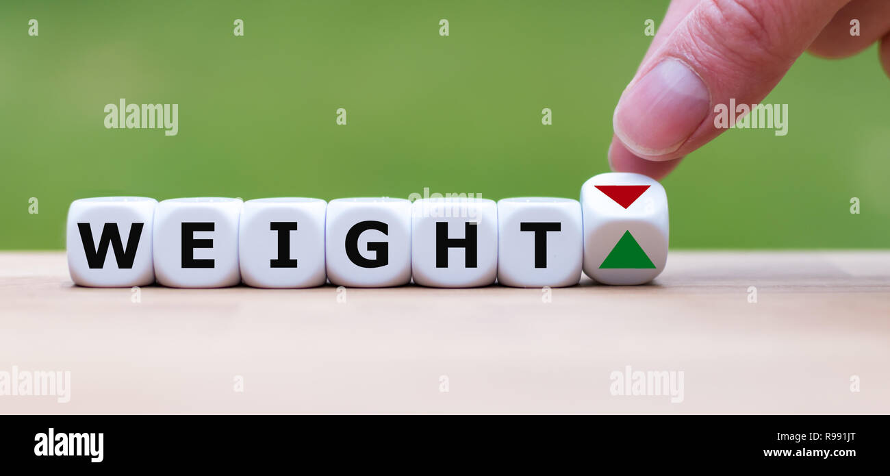 Hand is turning a dice and changes the direction of an arrow symbolizing to loose weight (or vice versa) Stock Photo