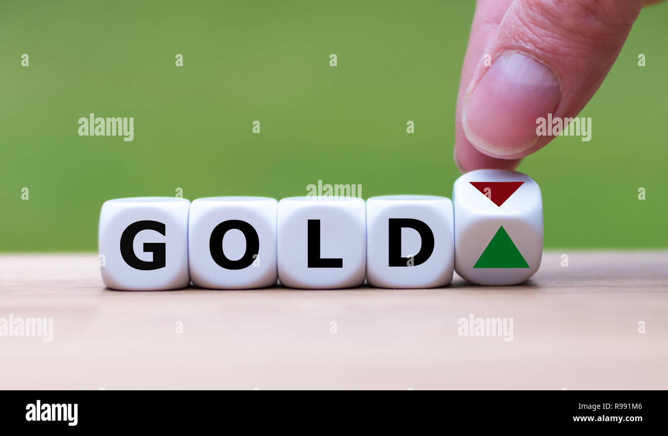 Hand is turning a dice and changes the direction of an arrow symbolizing that the price for gold is changing the trend and goes up instead of down (or Stock Photo