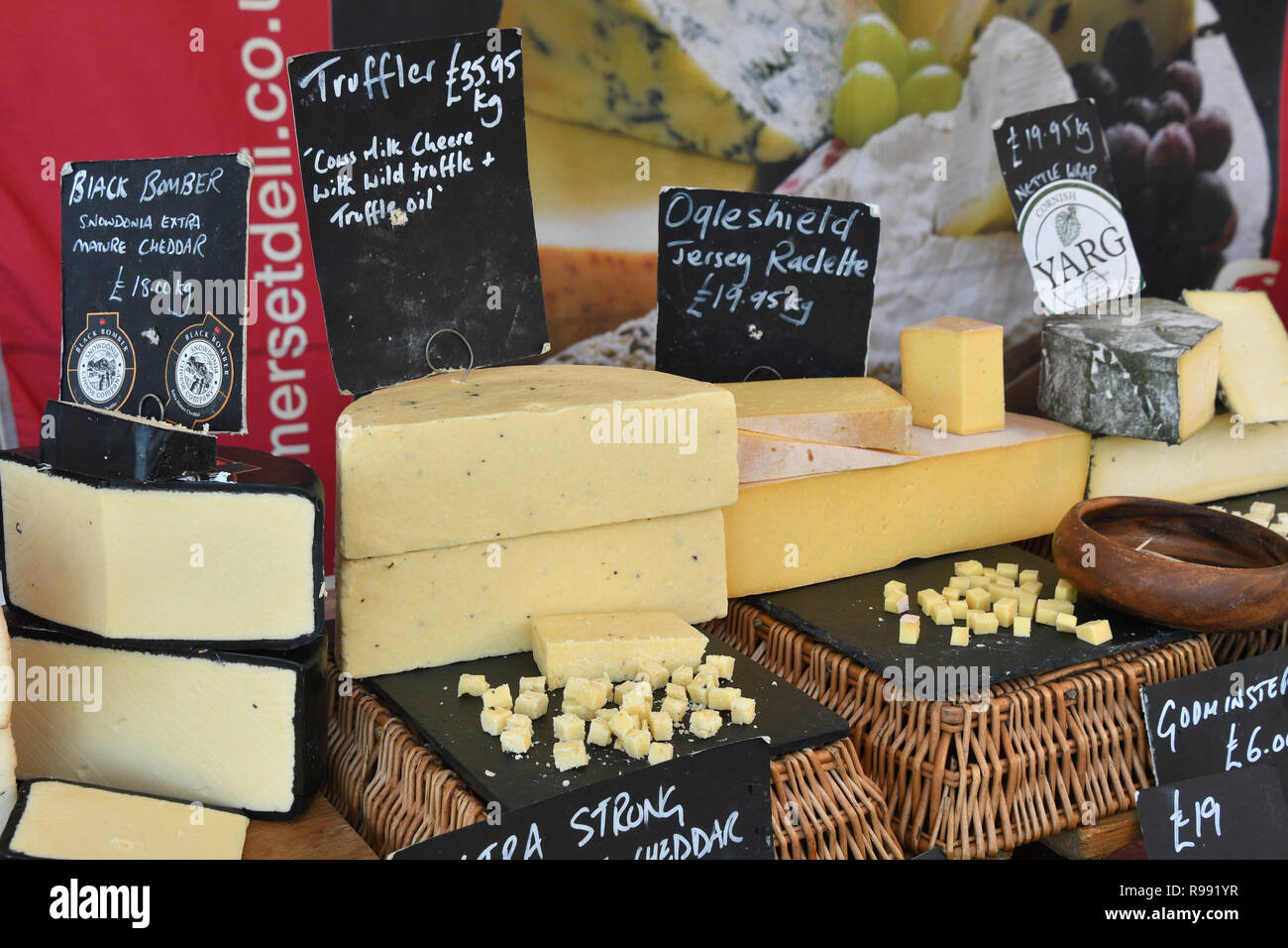 Cheeses on market stall in Somerset displayed with samples for tasting. Black BomberCheddar,Truffles,Ogleshield Jersey,Cornish Yarg nettle Wrapped,UK Stock Photo