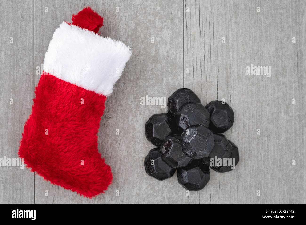 Red and white Christmas stocking and pile of coal shaped candy on a gray washed wood background, as a naughty for Christmas concept Stock Photo