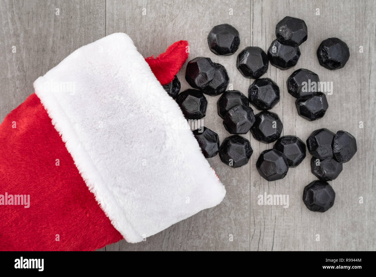 Traditional red and white Christmas stocking with coal shaped candy spilling out onto a gray washed wood background, a naughty for Christmas concept Stock Photo