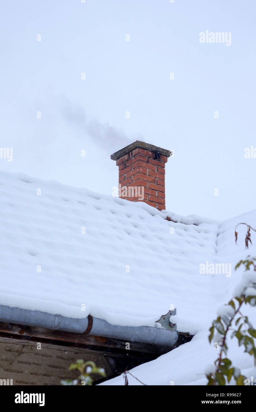 smoking chimney on a traditional house in a rural hungarian village covered in snow from a fresh snowstorm zala county hungary Stock Photo