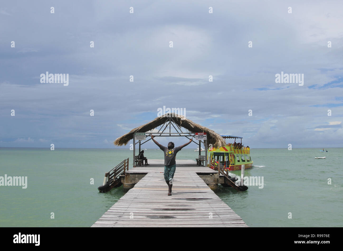 A jovial man dancing with raised arms in awe-inspiring spirits on wooden jetty after getting off a tour boat and expressing wonderful feelings of joy. Stock Photo