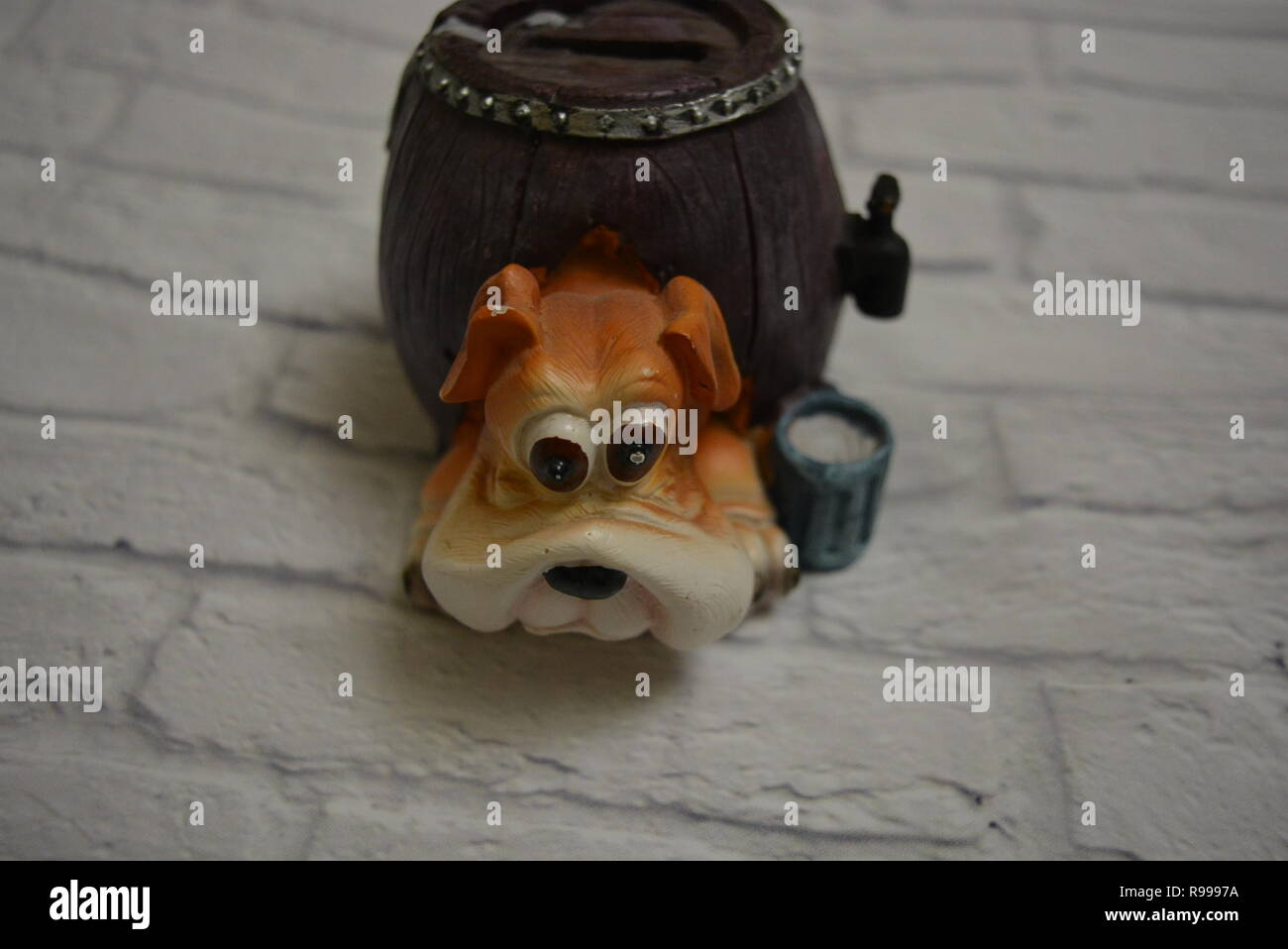 Ceramic drip tray in the form of a beer barrel with a dog head and a blue glass of beer next to it against the background of a white brick wall. Stock Photo