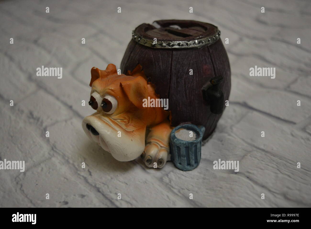Ceramic drip tray in the form of a beer barrel with a dog head and a blue glass of beer next to it against the background of a white brick wall. Stock Photo