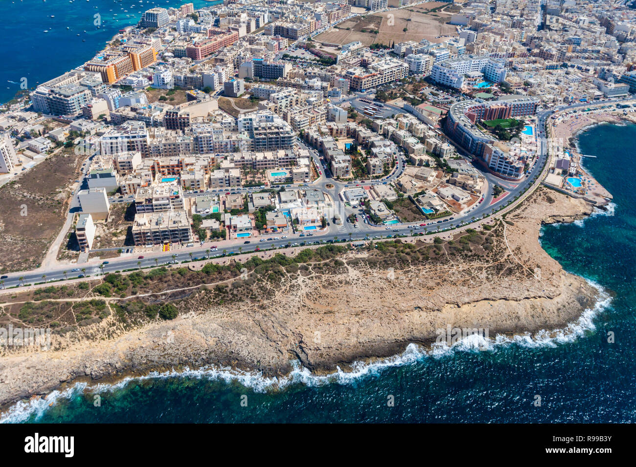 Seaside cliffs, colourful houses and streets of Qawra town in St. Paul's Bay area in the Northern Region, Malta. Popular tourist resort between Bugibba and Salina. Aerial view. Malta island from above Stock Photo