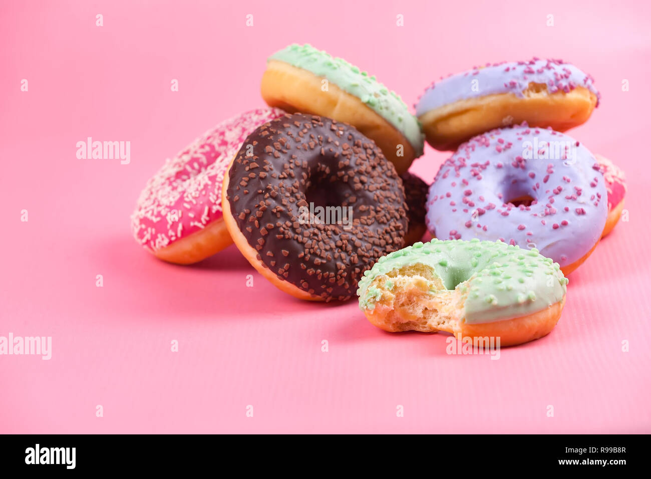 Sweet colorful tasty donuts with icing and sprinkles on pastel pink ...