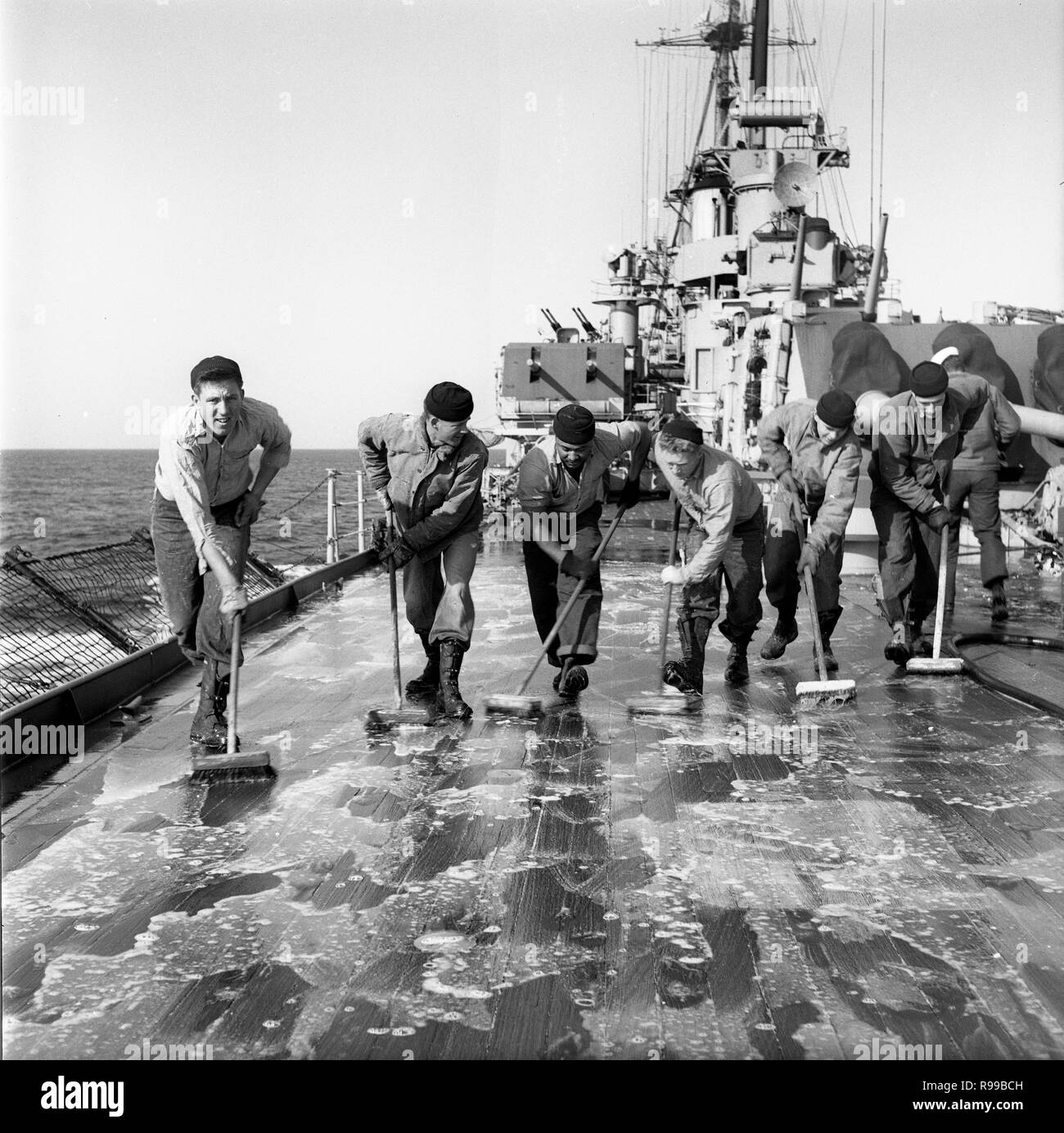 All hands on deck in 1950 as US Navy Sailors clean the deck of USS Rochester (CA -124) Cruiser Stock Photo