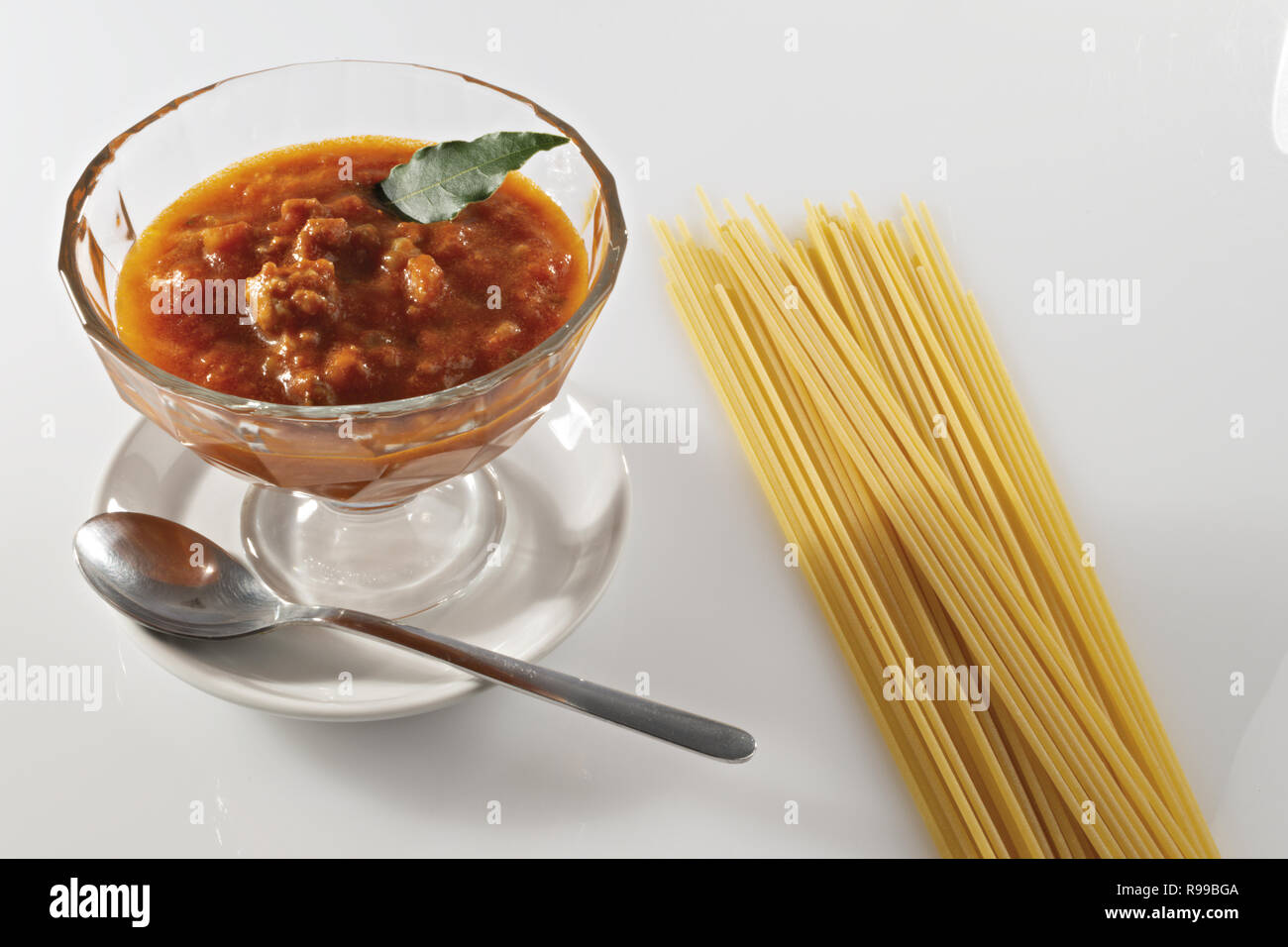 meat and tomato ragu in glass bowl and raw pasta from above Stock Photo