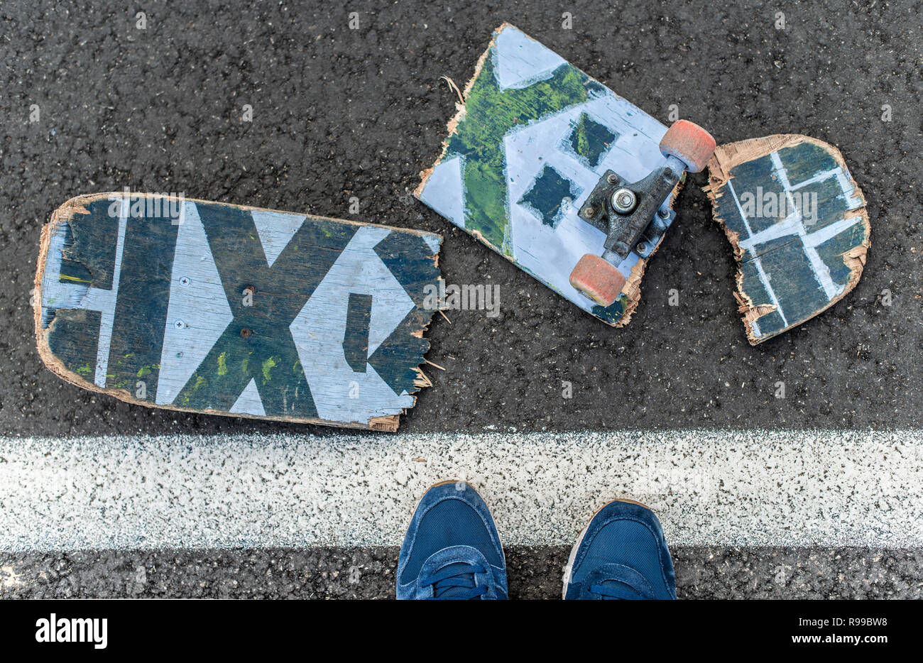 Broken skateboard on dark asphalt street. Boy with sneakers stepped on