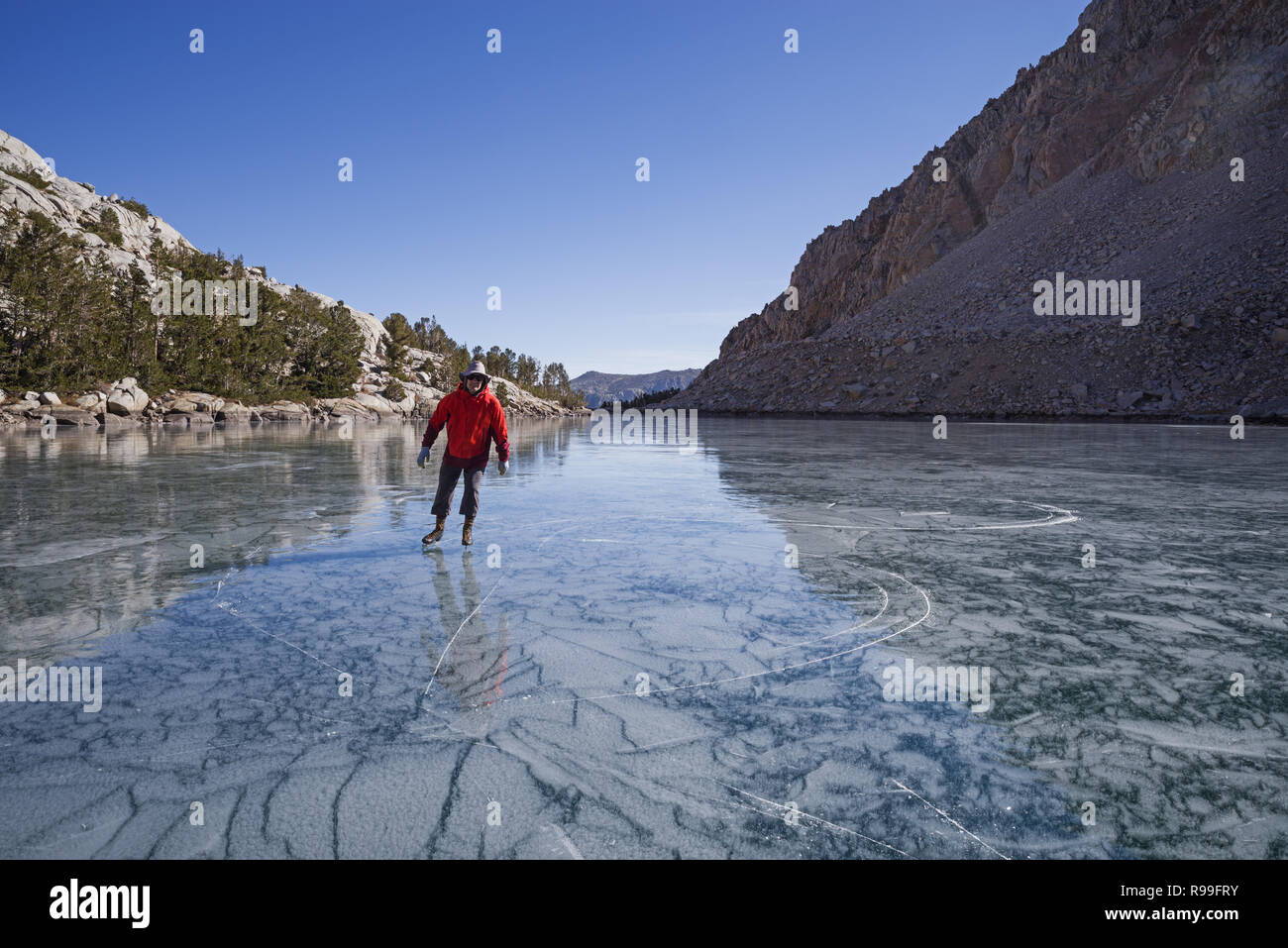 man in red jacket ice skating on frozen mountain lake Loch Leven in the Sierra Nevada Mountains Stock Photo
