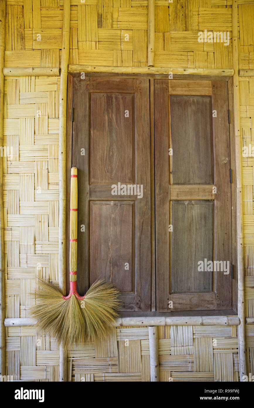 broom hanging on a bamboo bungalow wall with a shuttered window in Laos Stock Photo