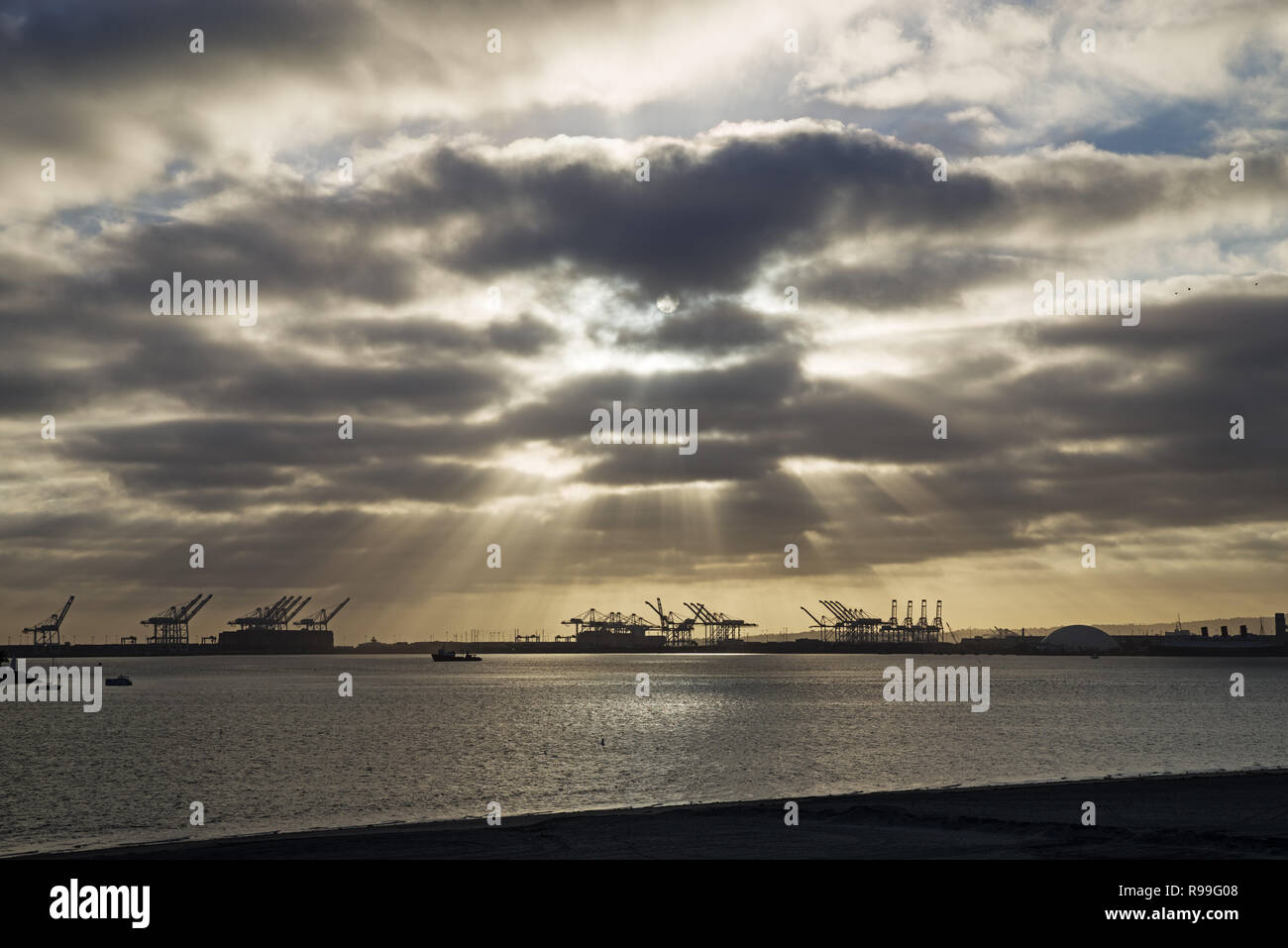 Long Beach in California with dramatic clouds and sunrays and crane and ship silhouettes Stock Photo
