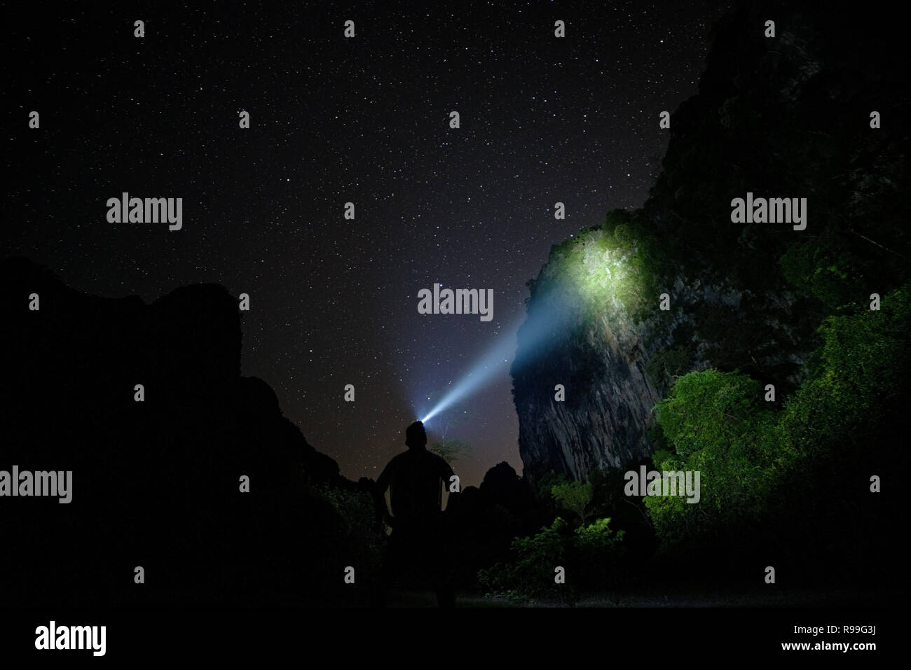 silhouette of a man with a headlight illuminating a cliff in Laos at night Stock Photo
