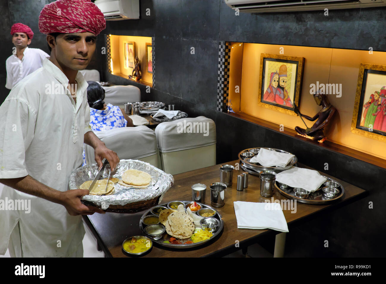 A waiter at Golden Star Rajasthani restaurant in Mumbai, fittingly clad in ethnic dress, serves the food on a traditional round metal plate or thali Stock Photo
